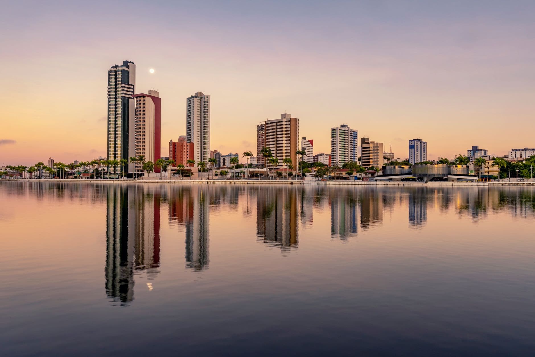 Picturesque scenery of coherent tall modern buildings of contemporary megalopolis near calm river in sunset in dusk