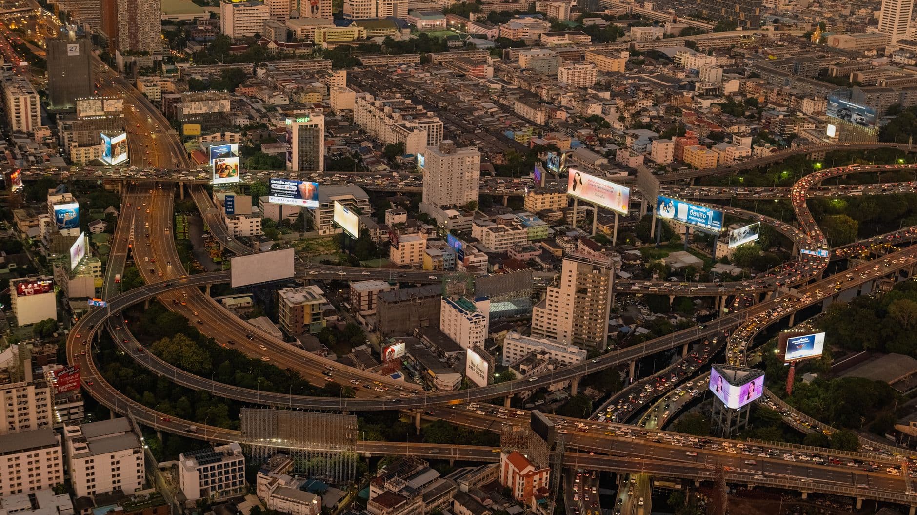 Aerial shot of a busy highway interchange with city skyline at dusk.