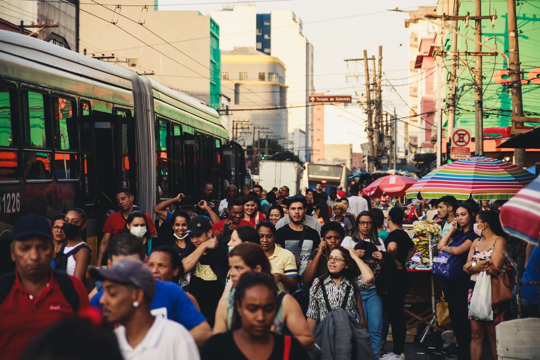 Busy urban street market featuring diverse crowd and public transportation.