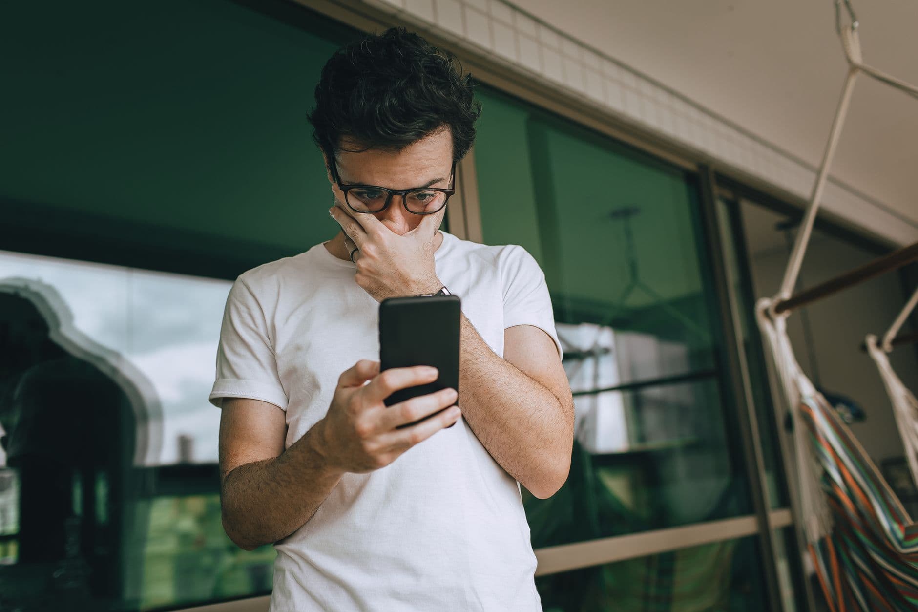 Man with eyeglasses focused on smartphone indoors, captured in a contemplative moment.