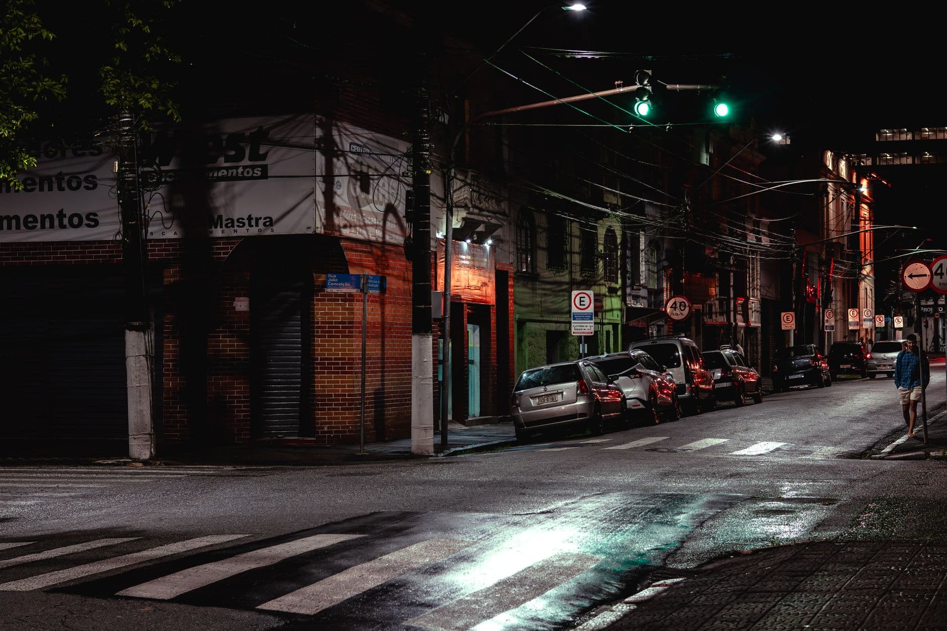 A quiet urban street at night with parked cars and wet reflections under streetlights.