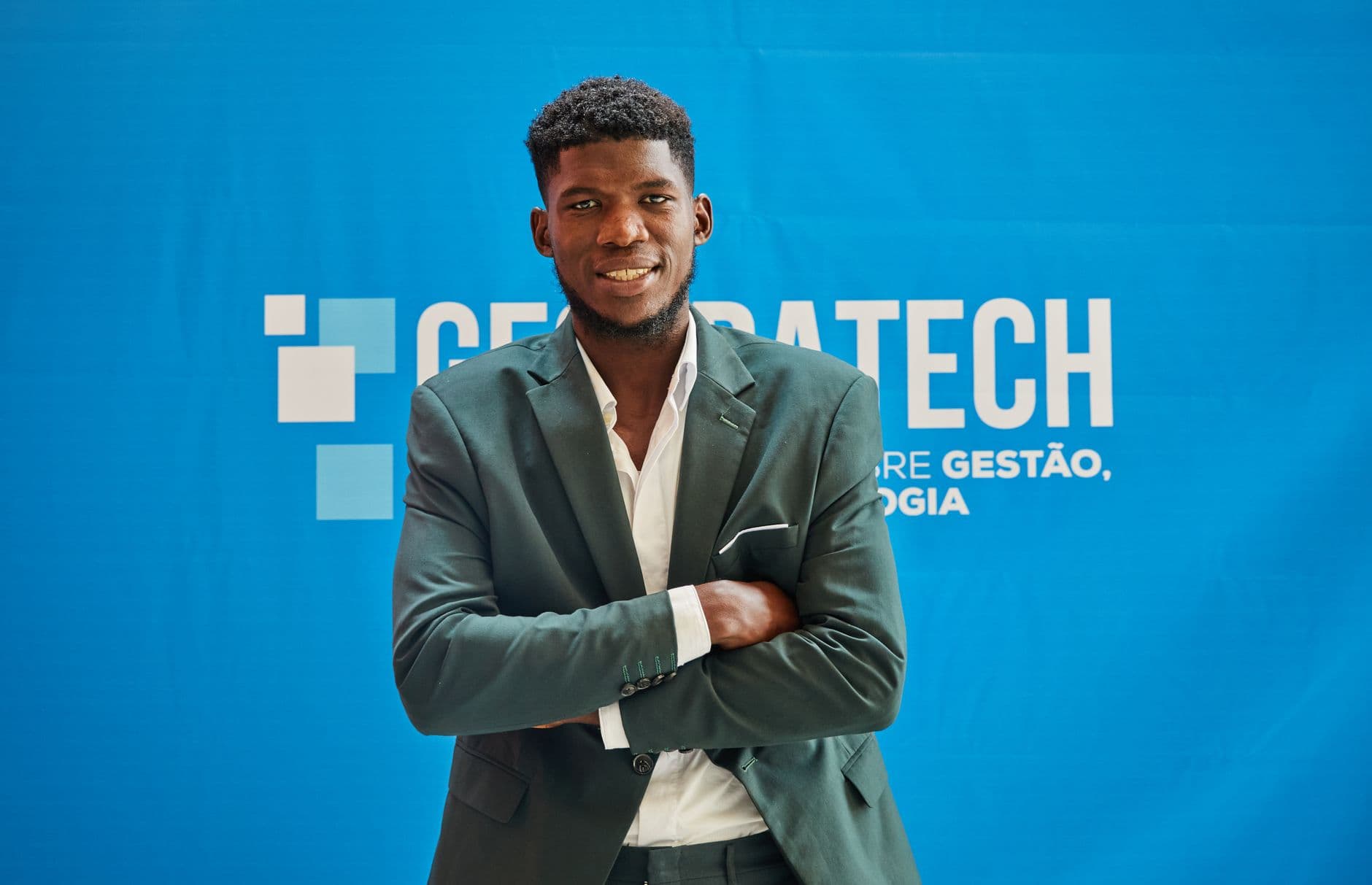 Businessman in suit smiling confidently with arms crossed at a technology event.