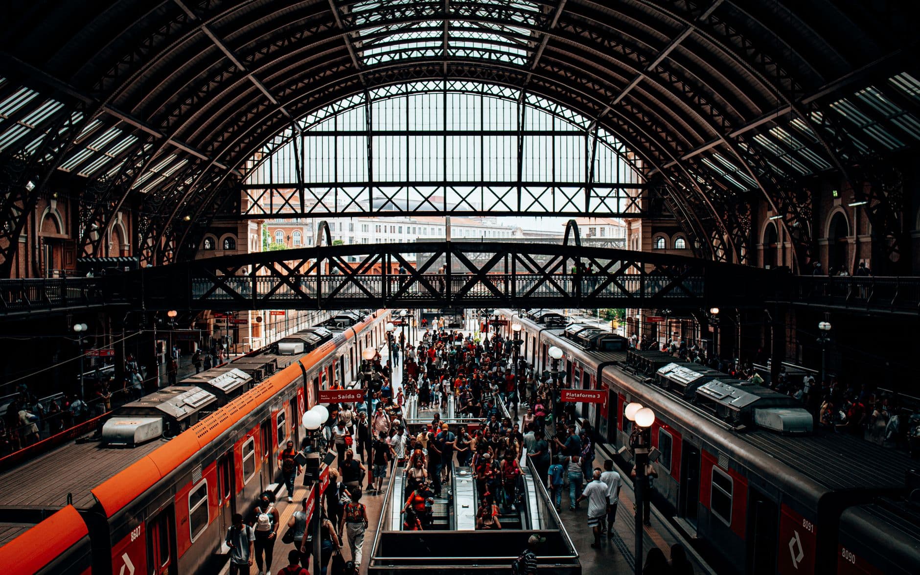 A bustling scene of people at a historic train station with arched roof and platforms.