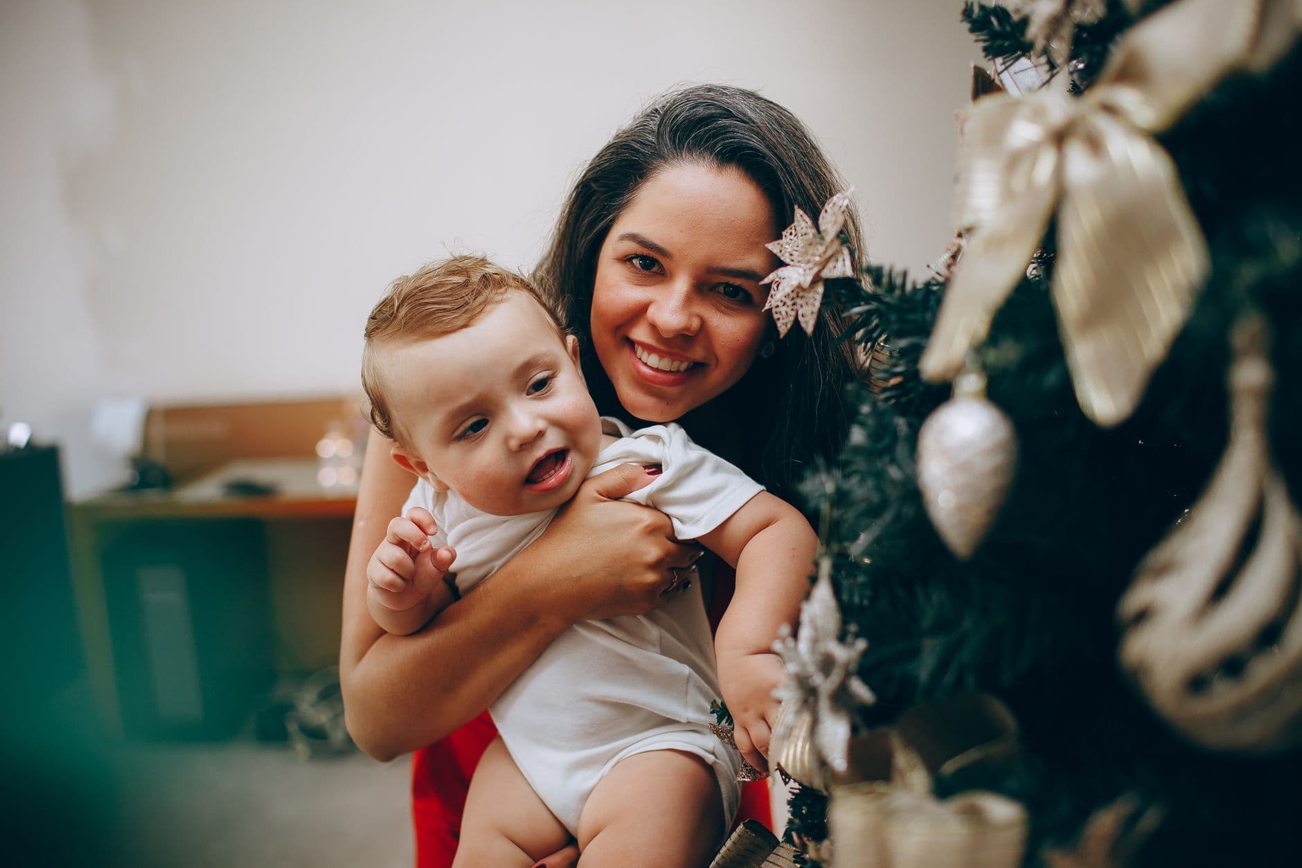 A joyful mother and baby enjoying festive moments by the Christmas tree indoors.